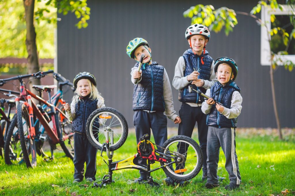 Children mechanics, bicycle repair. Happy kids fixing bike together outdoors in sunny day. Bicycle repair concept. Teamwork family posing with tools for repairing a bicycle in hands outside