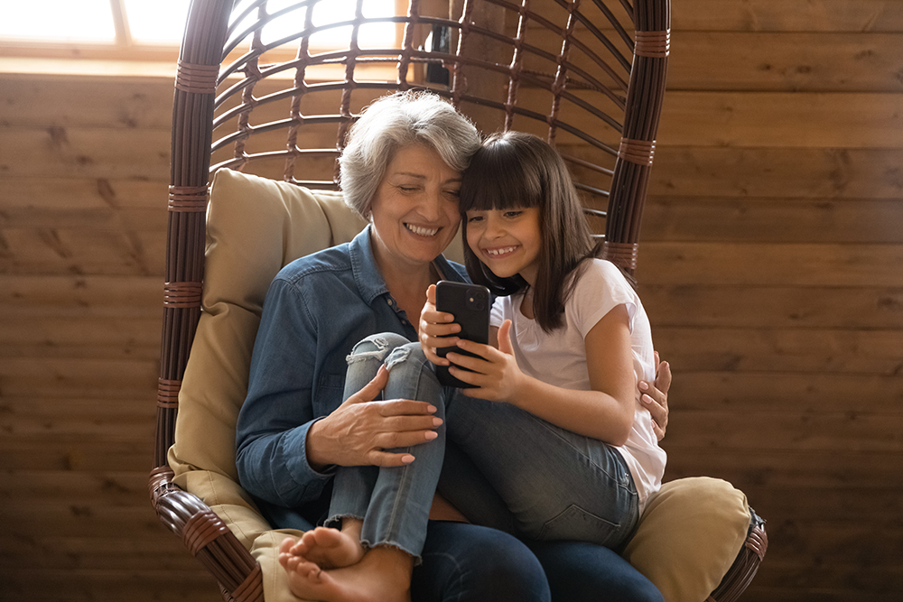 Happy senior grandmother and granddaughter use smartphone laughing
